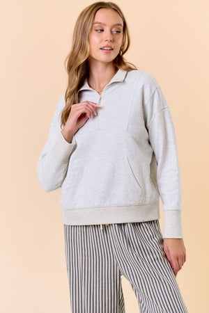 Woman wearing a light gray sweater and striped pants on a beige background