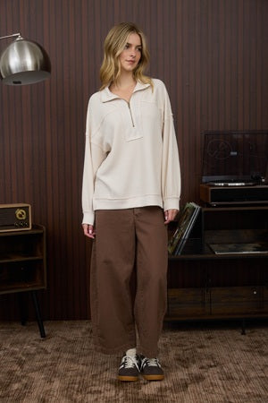Woman wearing a beige top and brown pants standing in a room with vintage decor.
