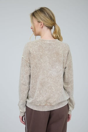 Woman wearing a beige sweater and brown pants against a plain background