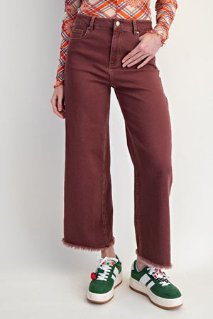 Person wearing brown wide-leg jeans with a colorful shirt and green sneakers on a white background