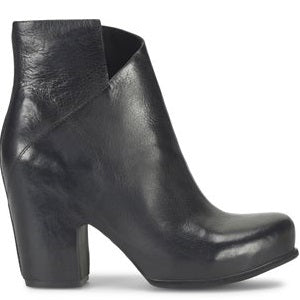 A black leather bootie with an asymmetric topline and a block heel, featuring a side zip closure and a cushioned footbed.