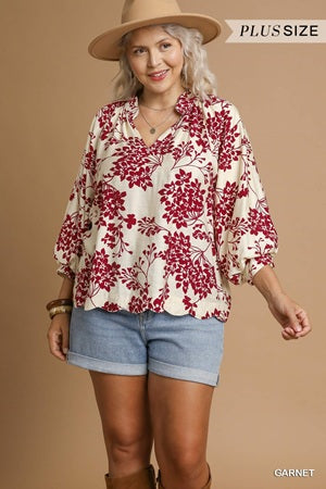Woman wearing a floral blouse, shorts, and a hat on a brown background