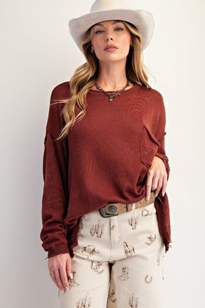 Woman wearing a rust-colored sweater and white pants with a pattern, standing against a plain background.