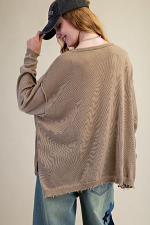 Person wearing a beige sweater and blue jeans with a plain background