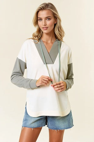 Woman wearing a color-blocked long-sleeve top with denim shorts on a plain background