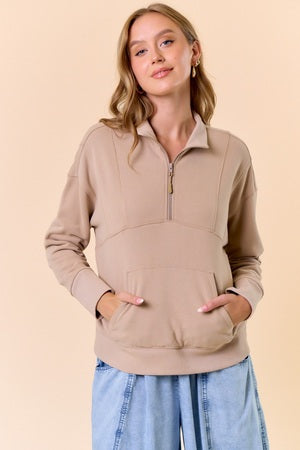 Woman wearing a beige zip-up sweatshirt with a plain background