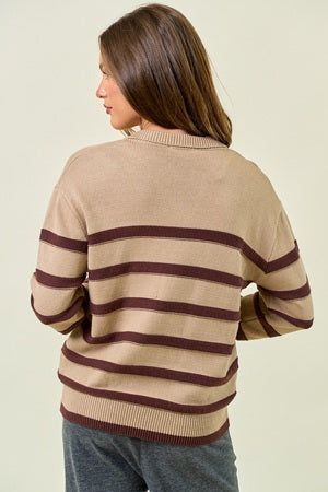 Woman wearing a beige sweater with brown stripes on a plain background