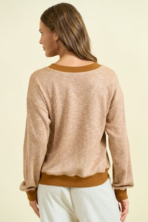 Woman wearing a beige and brown sweater with a plain background