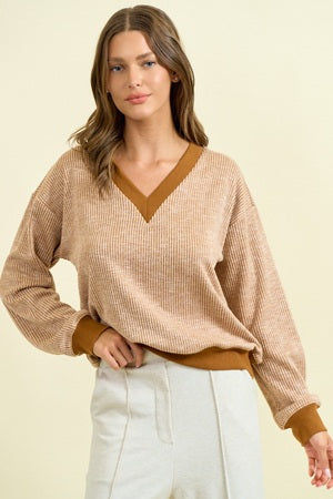 Woman wearing a beige sweater with a V-neck and brown trim on a beige background