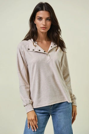 Woman wearing a beige long-sleeve shirt with button details and blue jeans on a light background