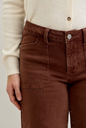 Brown pants worn with a cream sweater on a neutral background