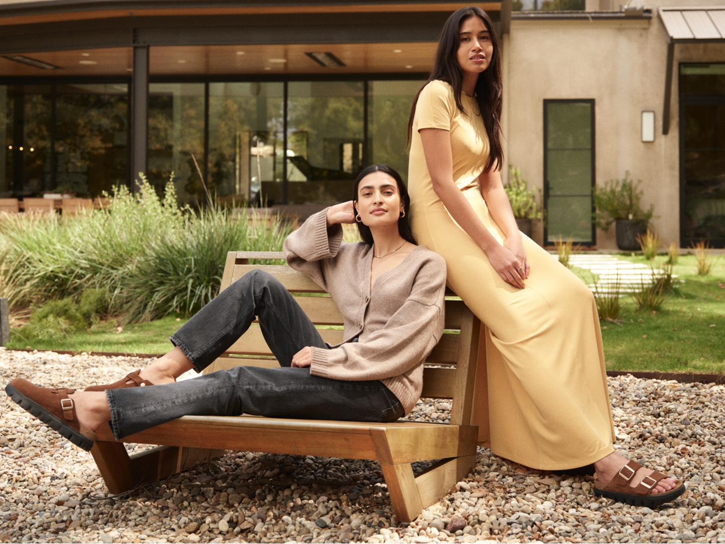 Two women sitting on a bench in front of a modern building.