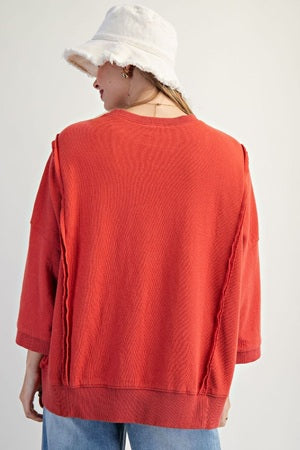 Person wearing a red textured sweater and white cap on a plain background