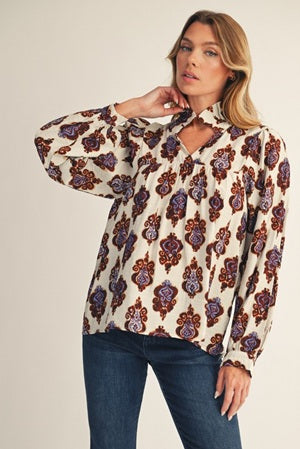 Woman wearing a patterned blouse and jeans against a plain background