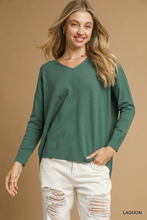 Woman wearing a green sweater and white jeans against a brown background