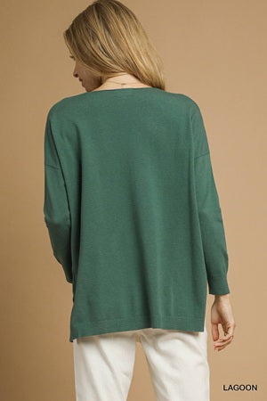 Person wearing a green sweater and white pants on a beige background