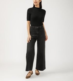 Person wearing a black turtleneck and wide-leg jeans on a white background
