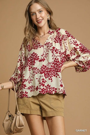 Woman wearing a floral blouse and shorts with a beige handbag on a brown background