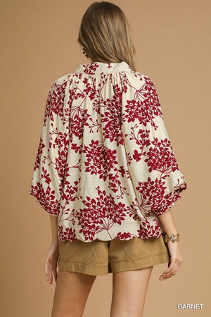 Woman wearing a floral blouse with red and white pattern on a beige background