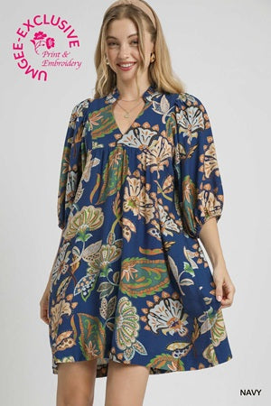Woman wearing a blue patterned dress with 'Macey Exclusive' branding on a white background