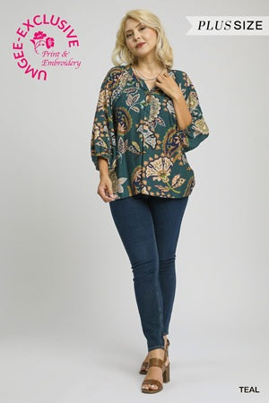 Woman wearing a teal plus-size printed top and blue jeans on a white background