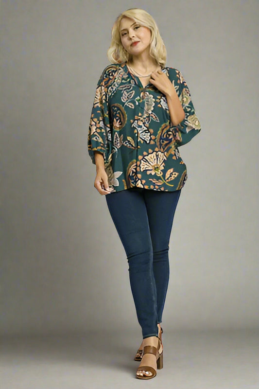 Woman wearing a teal plus-size printed top and blue jeans on a white background