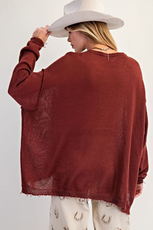 Person wearing a burgundy sweater and white hat on a plain background