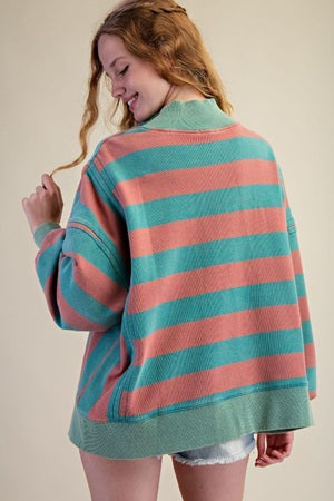Person wearing a striped sweater with pink and green horizontal stripes on a plain background
